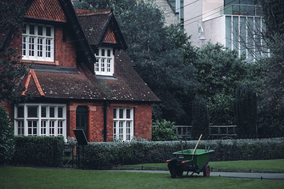 A cozy red brick house surrounded by greenery with a green wheelbarrow in the garden.