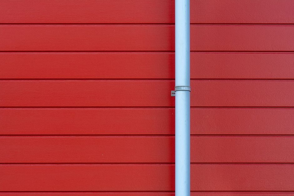 A minimalist photo of a red wall with a white rain gutter, showing clean lines and vibrant color contrast.